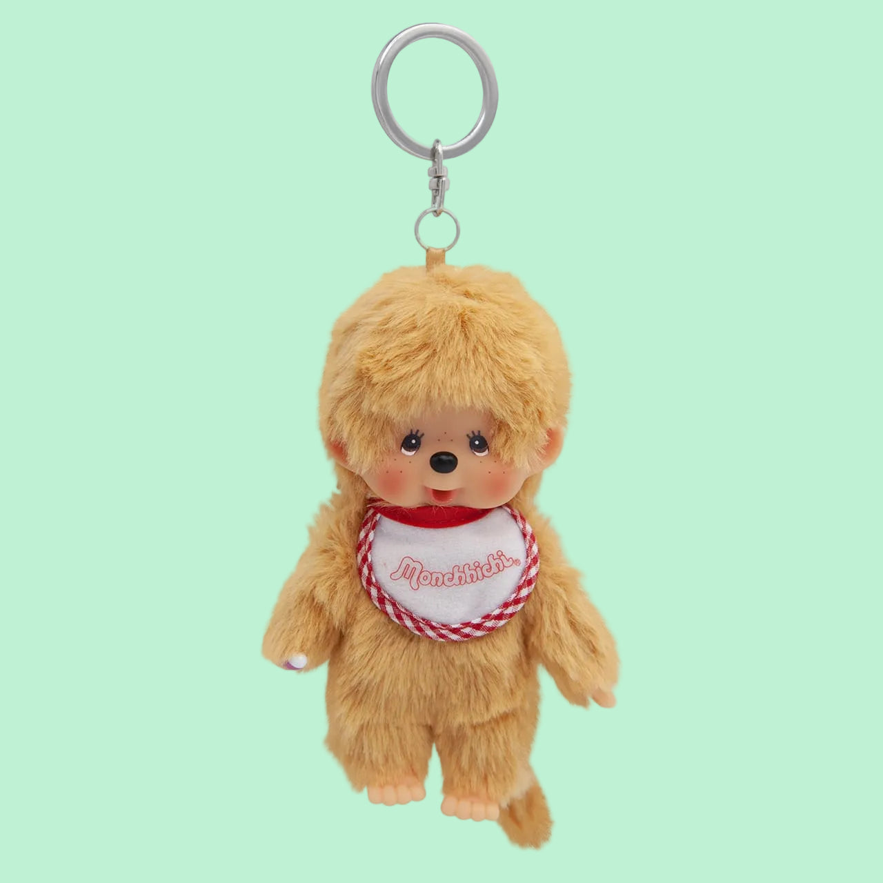 A beige Mochhichi monkey keychain wearing a bib that says Monchhichi.