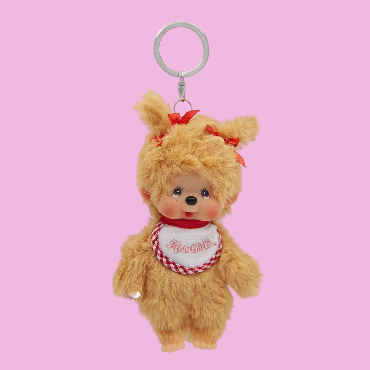 A beige Mochhichi monkey keychain wearing a bib that says Monchhichi. She has a red bow in her hair.