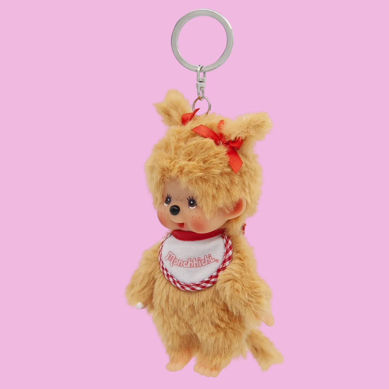 A beige Mochhichi monkey keychain wearing a bib that says Monchhichi. She has a red bow in her hair.