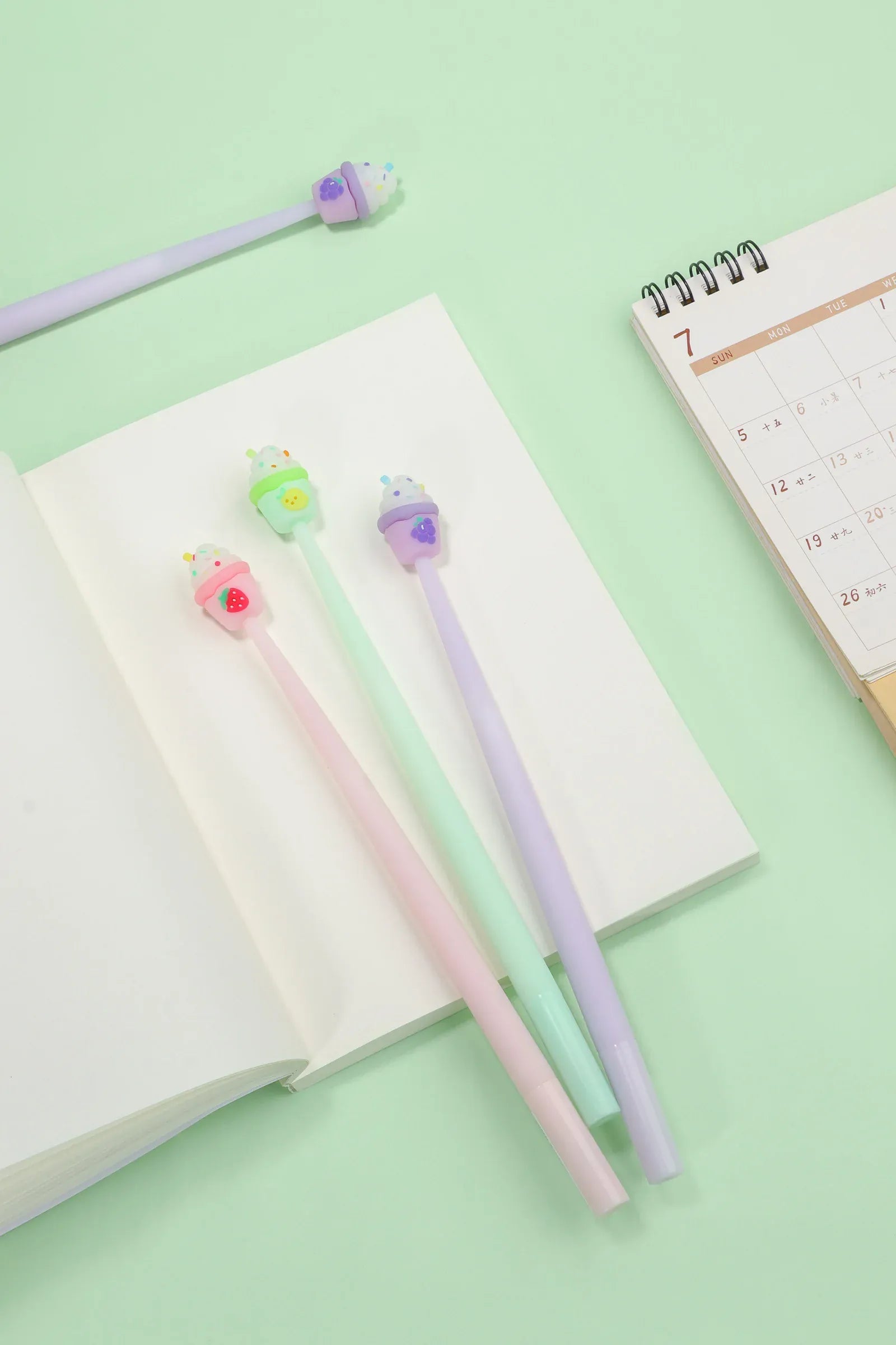 Several pens with cupcake toppers resting on a notebook.
