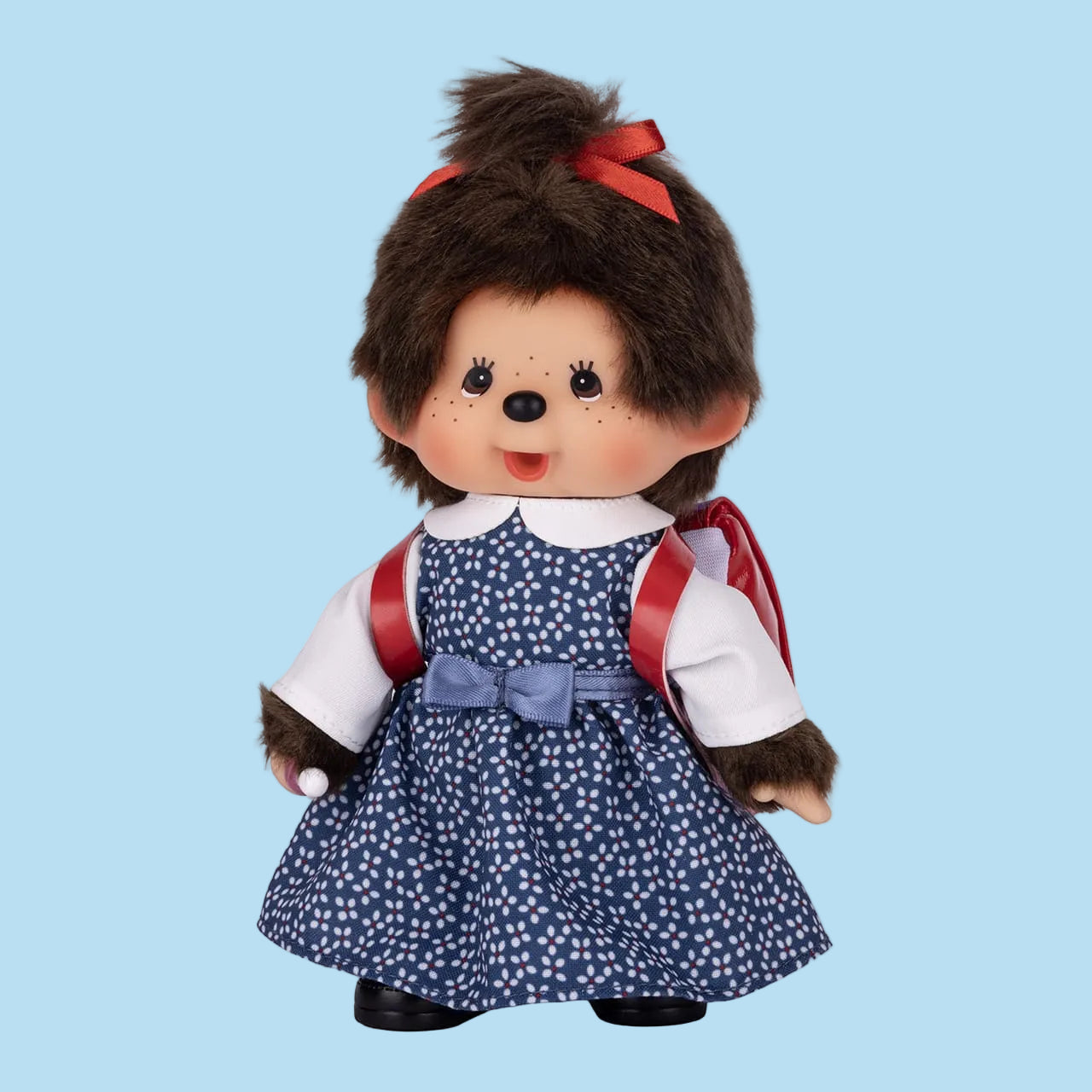 A Monchhichi plush wearing a blue dress with white polka dots, and a red backpack.
