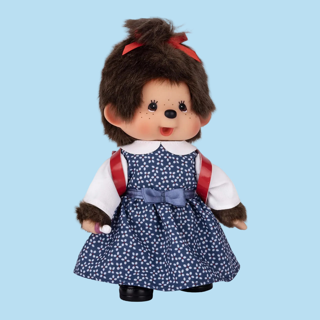 A Monchhichi plush wearing a blue dress with white polka dots, and a red backpack.