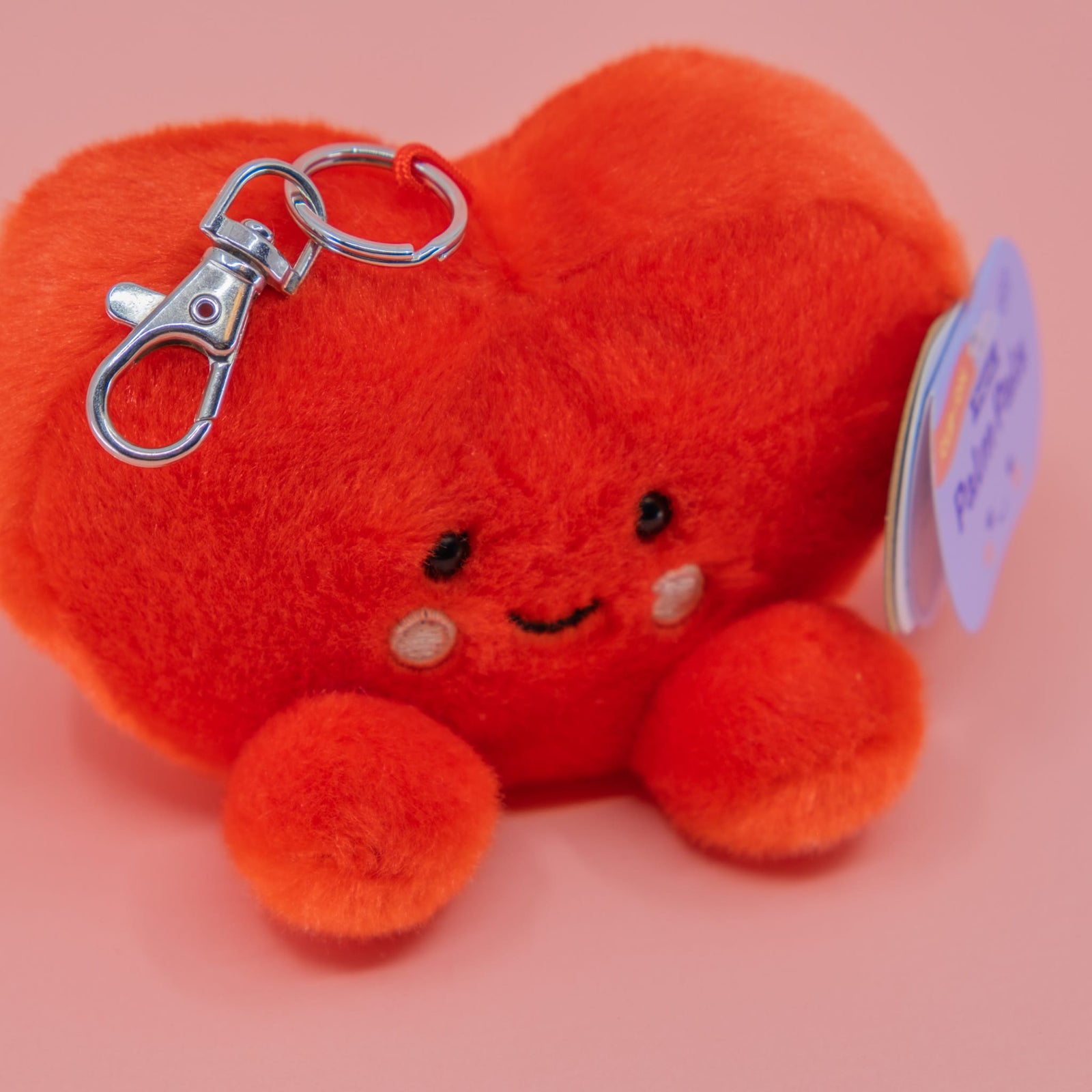 A cute heart plush key chain. It has a smiley face and round, little feet.