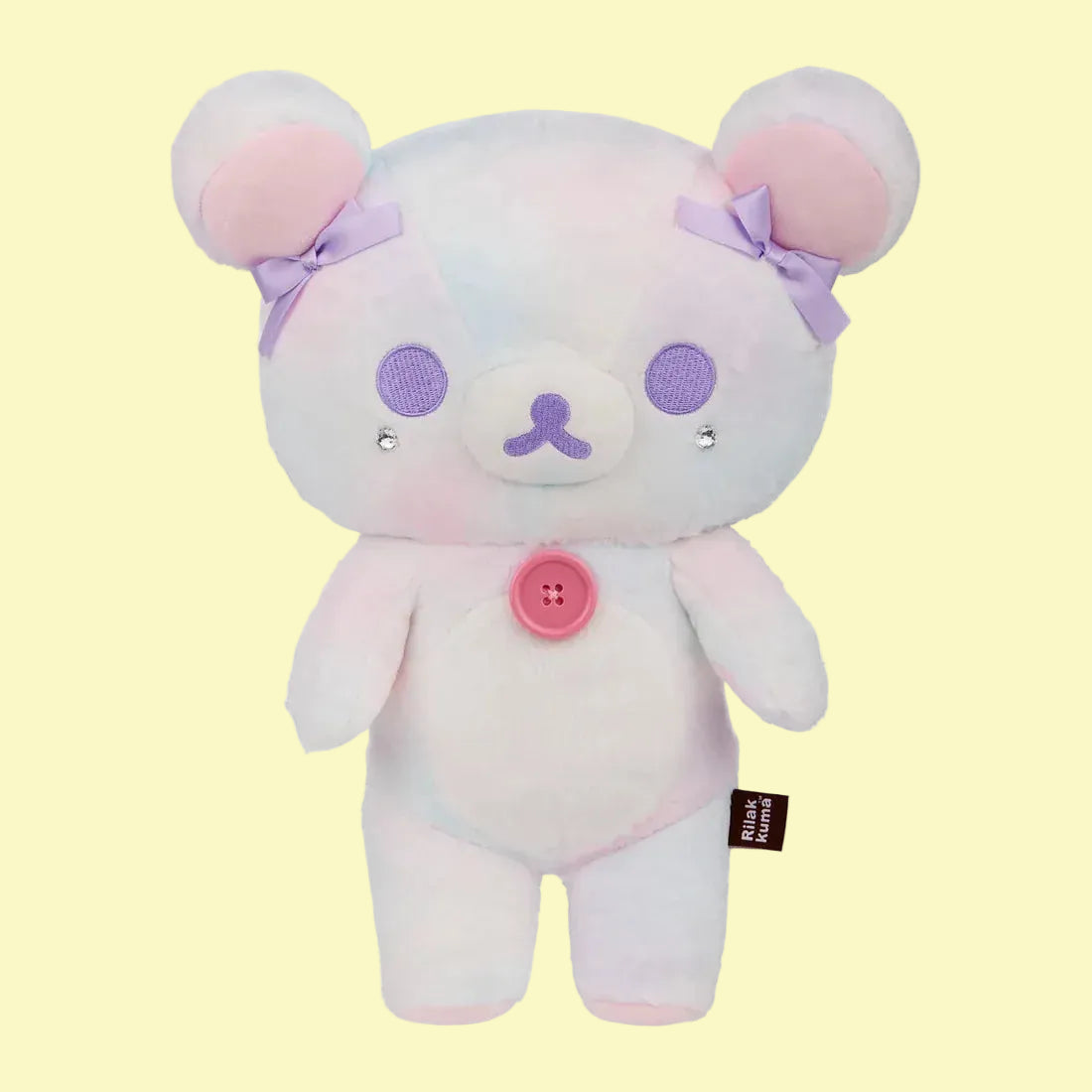 A white bear plush with purple bows on its ears and a pink button its chest.