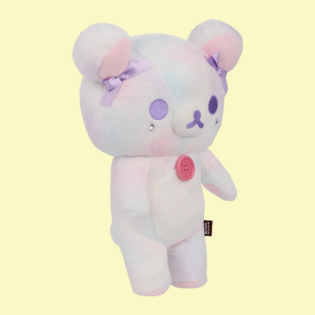 A white bear plush with purple bows on its ears and a pink button its chest.