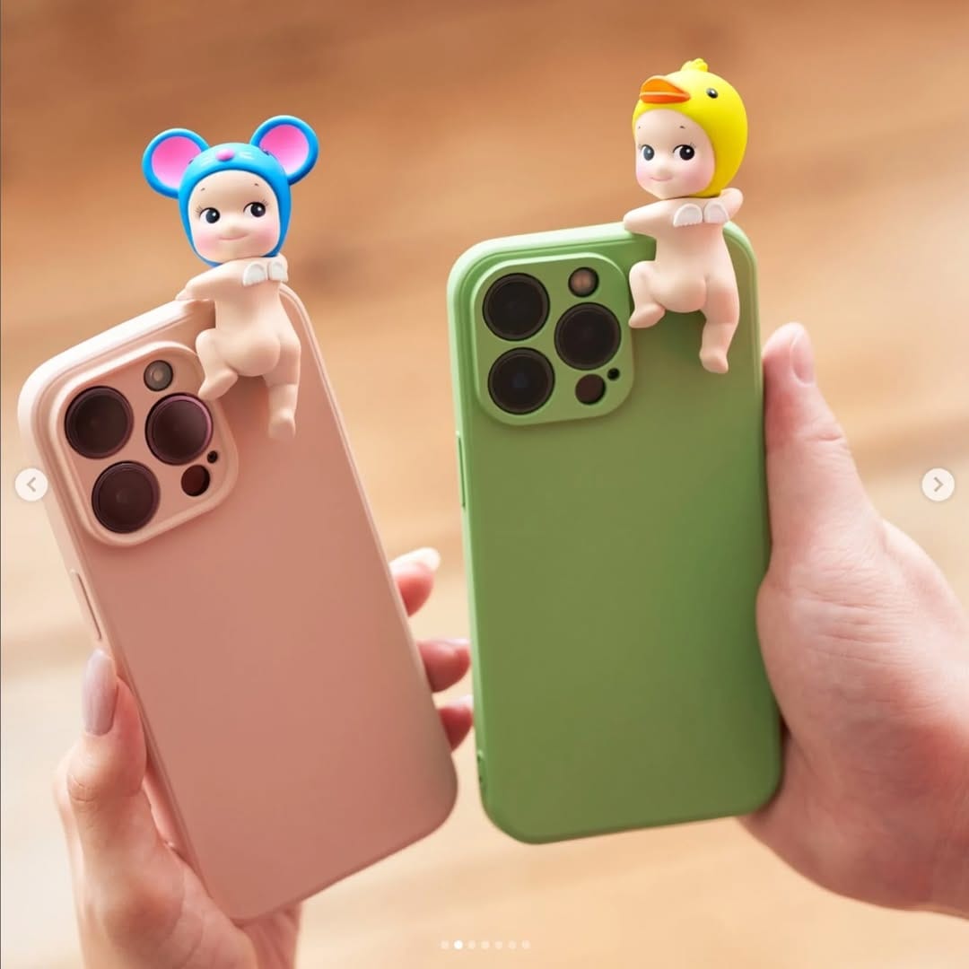 Mouse Sonny Angel Looking Back Hipper mounted on a pink cell phone case next to Duck Sonny Angel Looking Back Hipper mounted on a green cell phone case