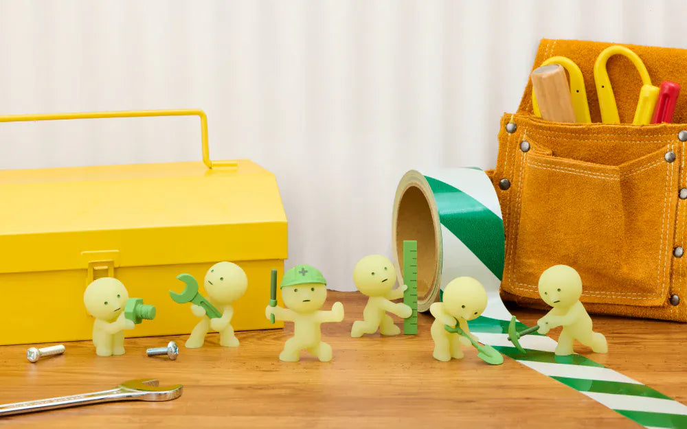 Many different Smiskis arranged around a toolbox. They are all construction themed, and are holding various oversized tools like wrenches, rulers, and shovels.