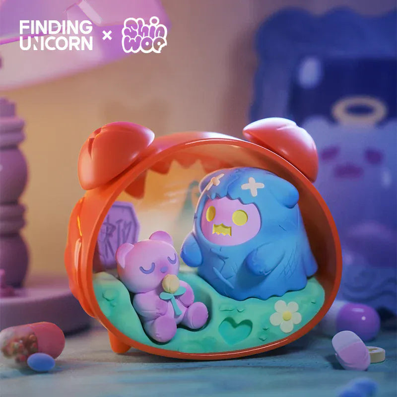 A figurine of a pink ghost wearing a blue bear skin inside a toy alarm clock. There is a second figurine of a  pink bear plush holding a flower also inside the alarm clock.