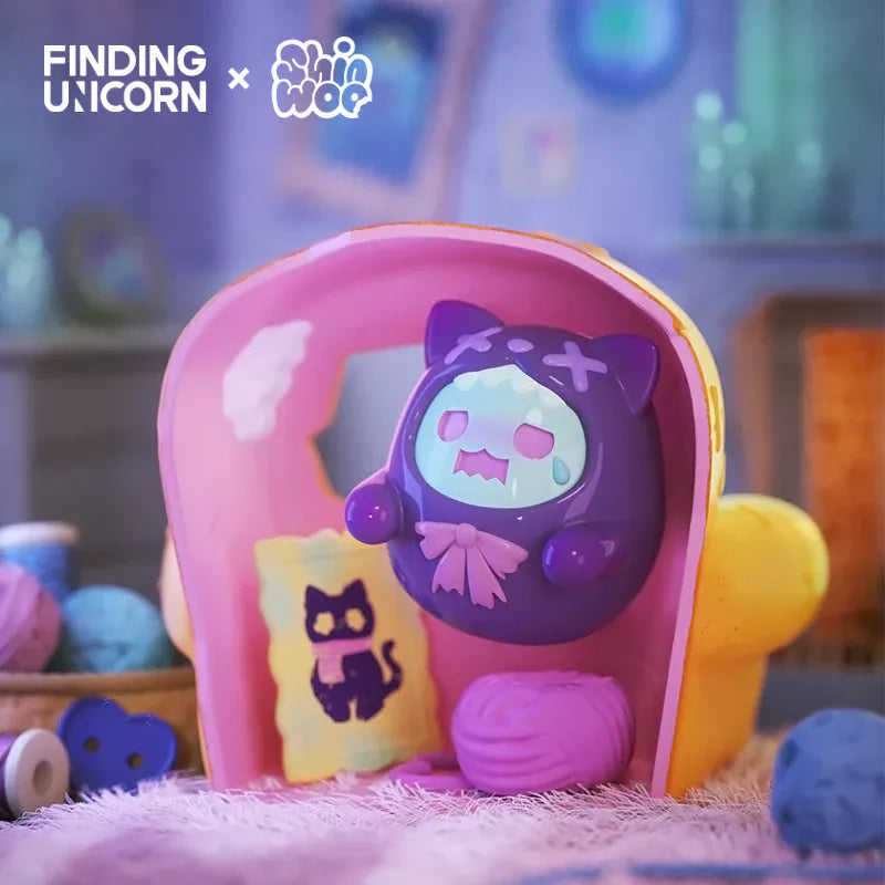 A figurine of a ghost wearing a cat skin inside a pink box. The ghost is crying and floating above a spool of yarn.
