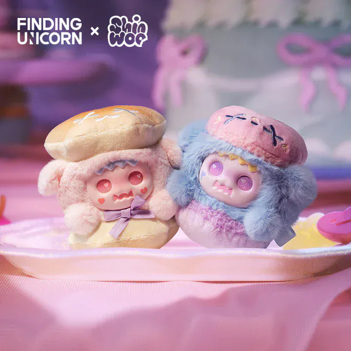 Two plushies of ghosts in bear skins. The ghosts are in between plush bread buns like a burger. The one on the left is pink and the one on the right is blue.