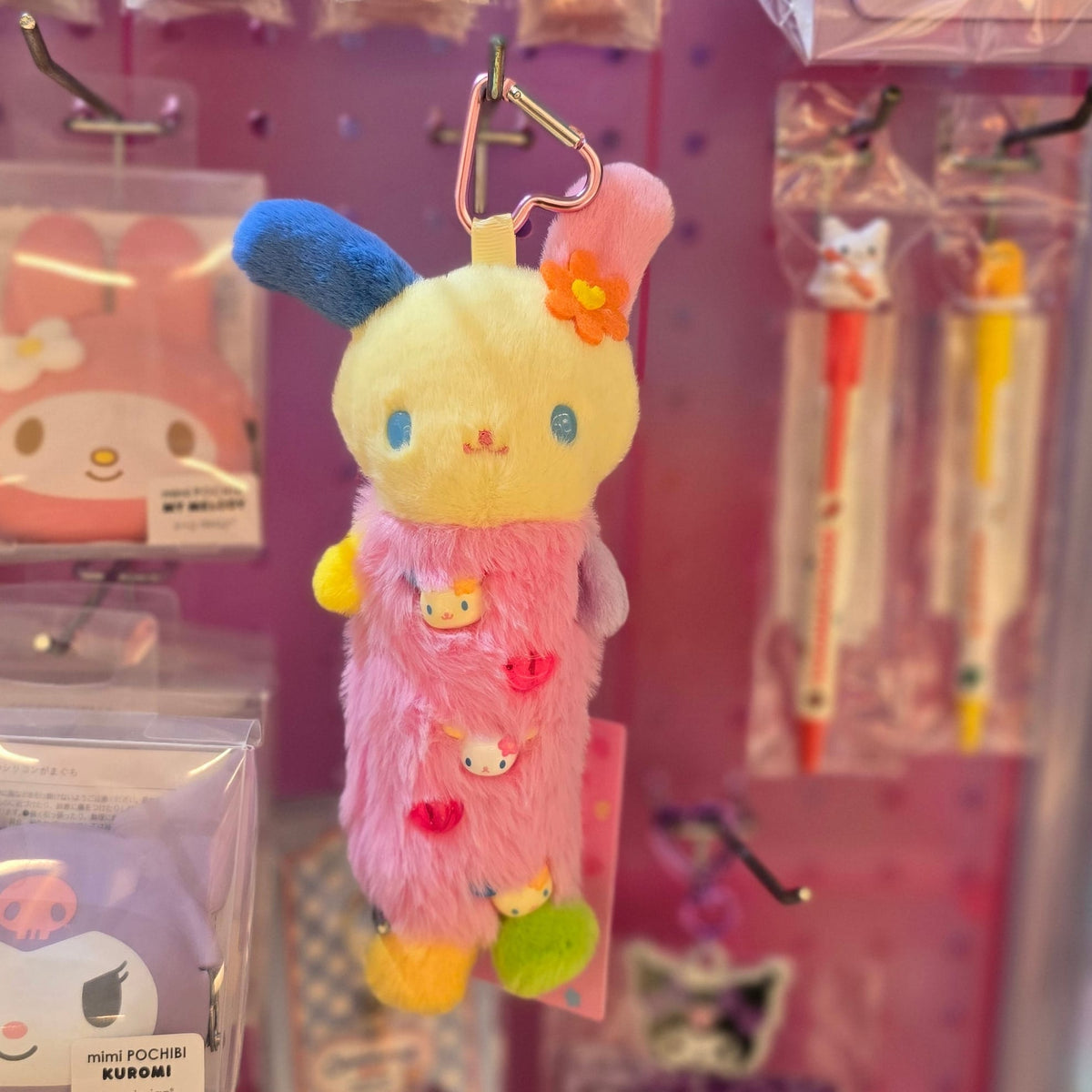 A colorful rabbit plush key chain with a long tube shaped body. It has Hello Kitty Faces on its body.