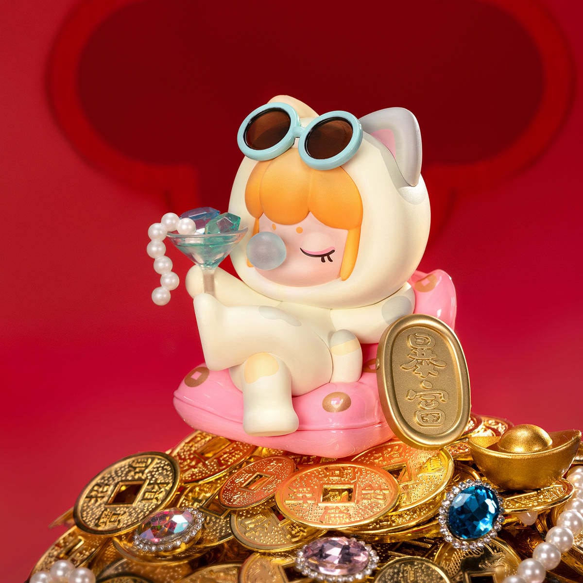 A figure of a little girl in a cat onesie. She is sitting on a pile of coins and has a drink full of pearls and jewels.
