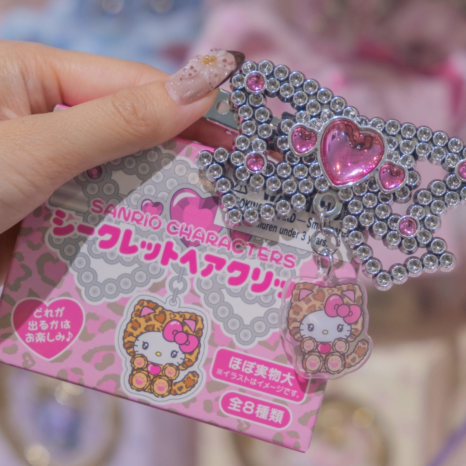 A hair clip shaped like a bow made of glittery beads. There is a cute Hello Kitty charm attached.