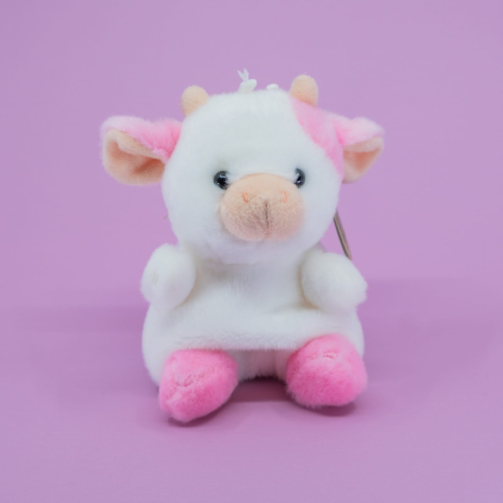 A cute plush of a cow with pink ears and pink feet.