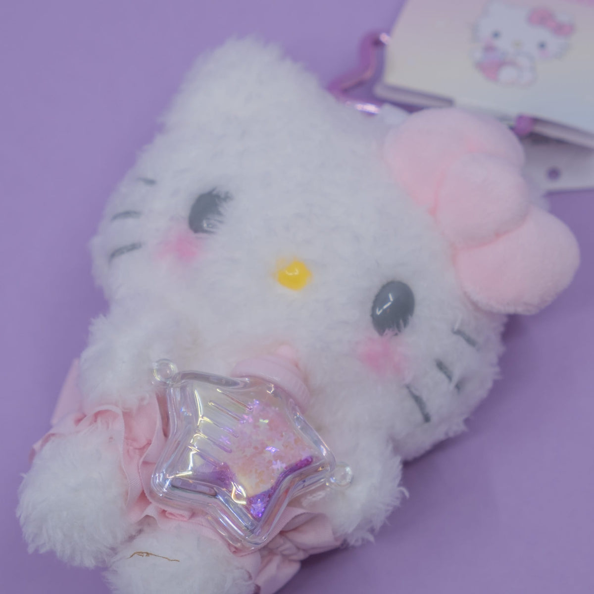 A Hello Kitty plush key chain. She is holding a small star shaped bottle.