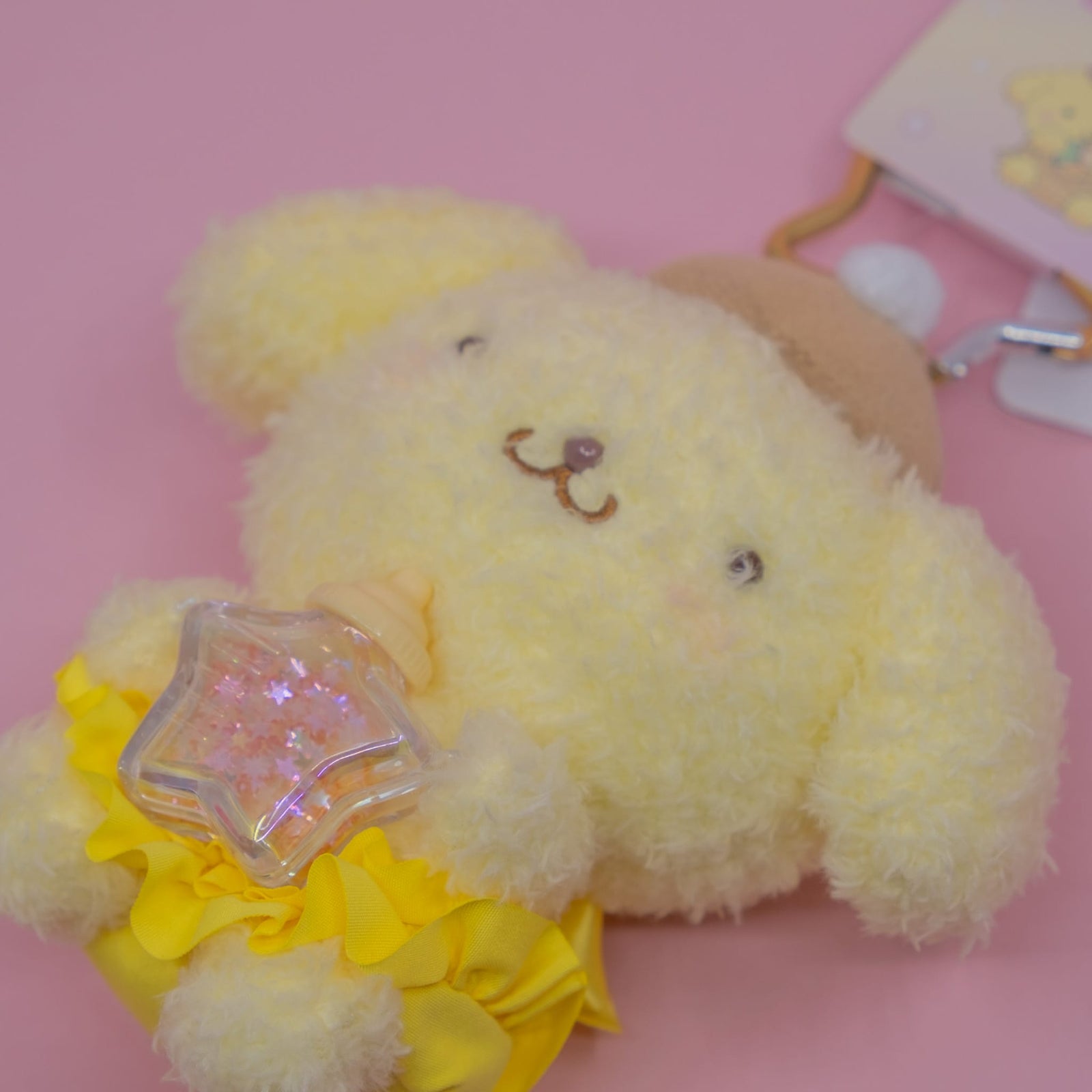 A yellow Pompompurin plush key chain. He is holding a small star shaped bottle.