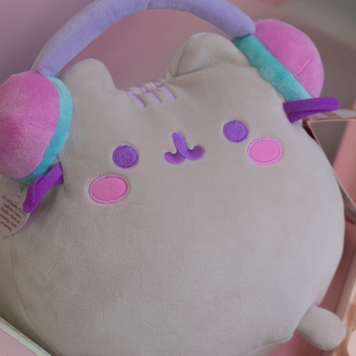 A large plush of a cat with a simple face wearing headphones.