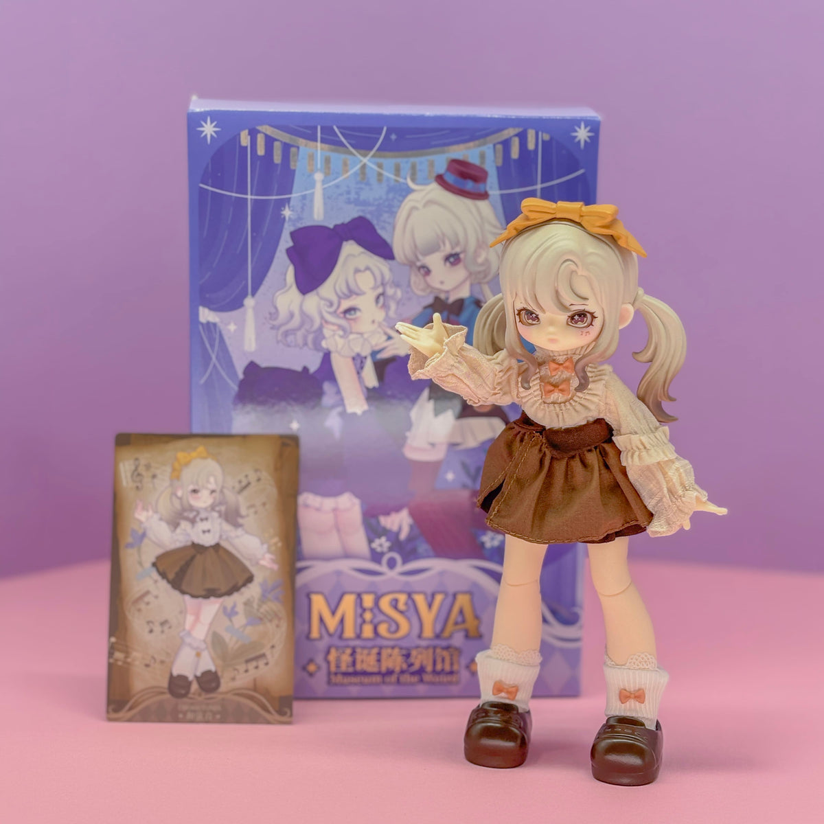 A figurine of an animal girl with grey hair wearing a yellow bow and a brown skirt. There is a box behind her with text reading "Misya".