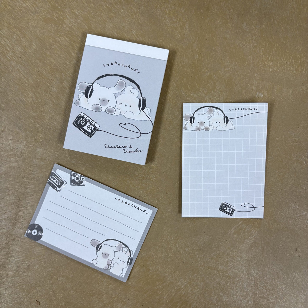 Various pages from a small notepad which has illustrations of two cute rabbit characters sharing a pair of headphones.