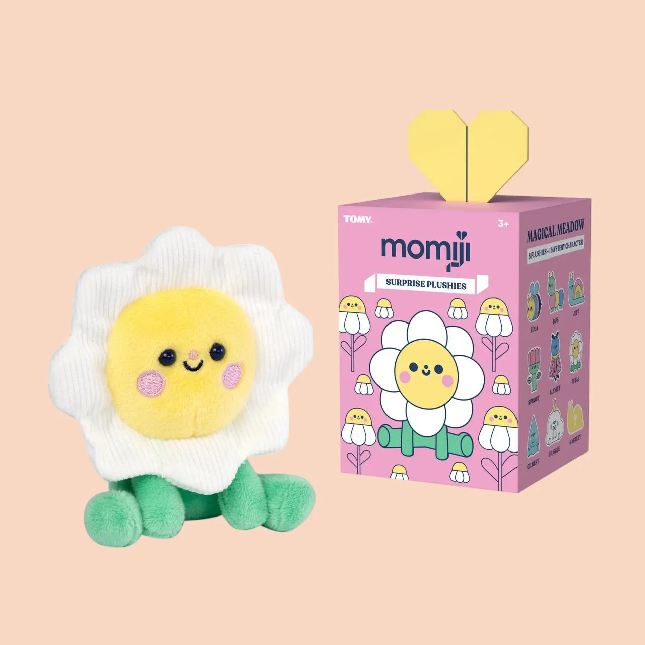A cute flower plush with a smiley face sitting beside a pink Momiji Magical Meadows blind box.