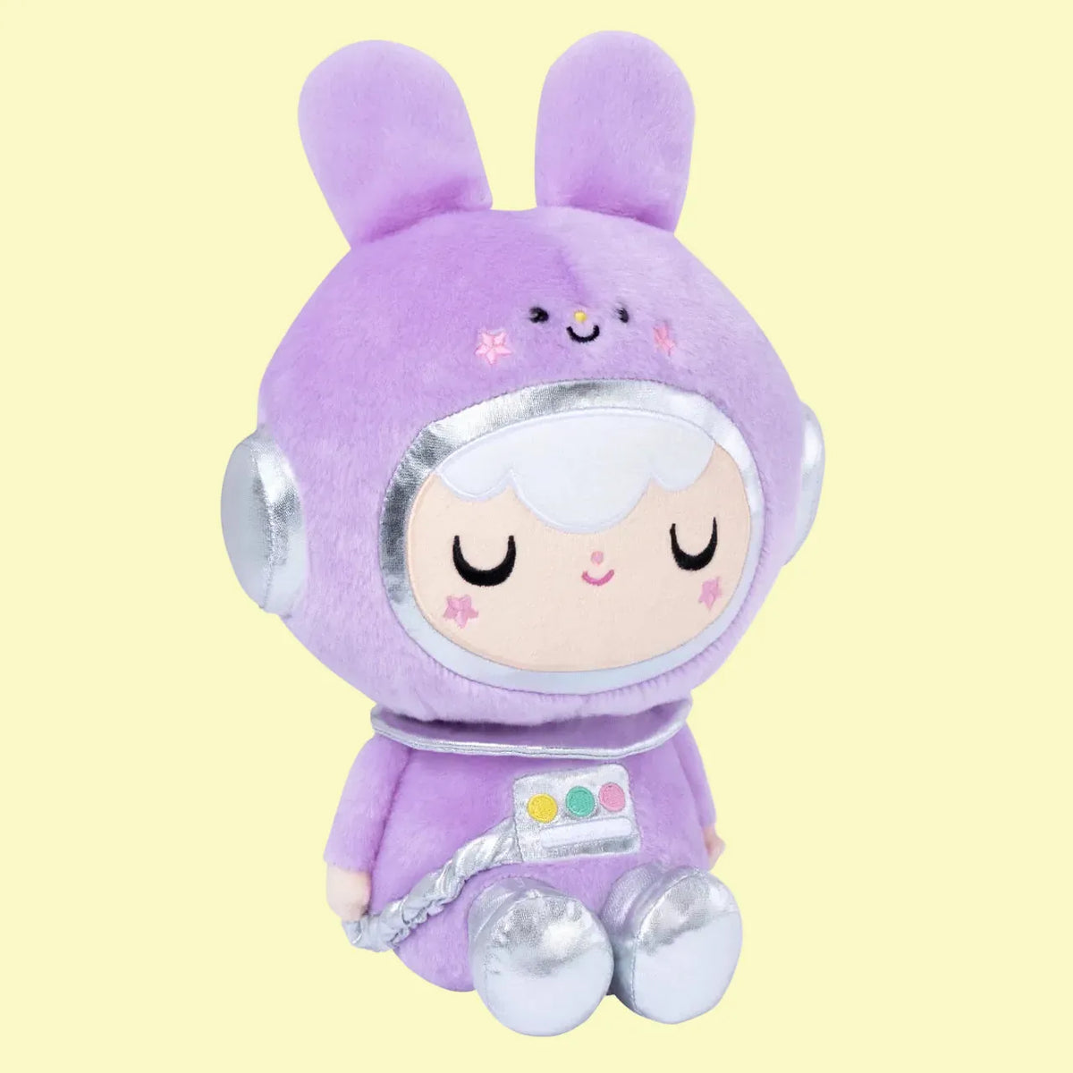 A cute plush of a girl in a purple, space themed, bunny outfit. She is sitting on the floor and smiling.