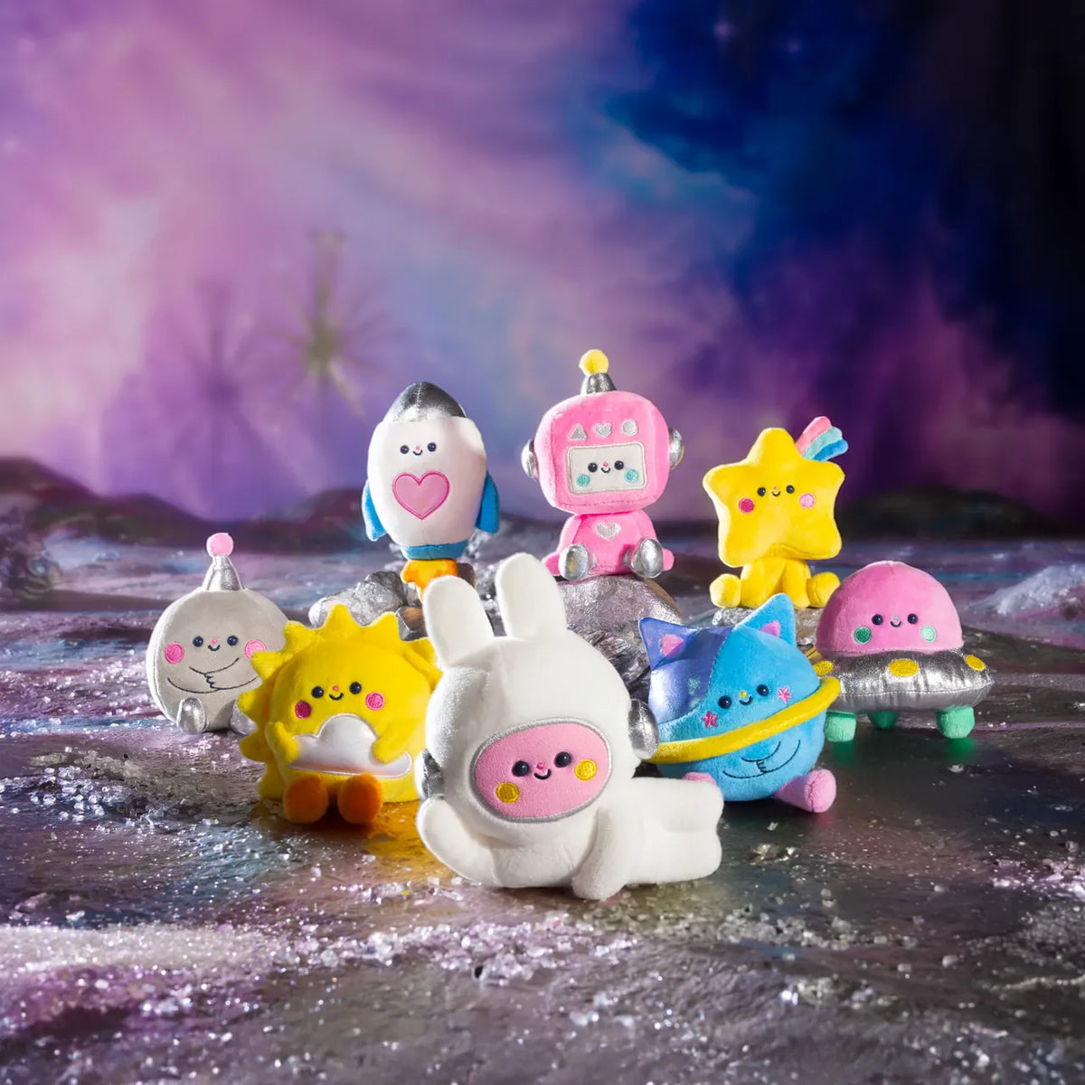 A collection of cute space themed plushies. There is a rabbit in a space suit, a smiling sun, and a happy rocket ship, as well as others.