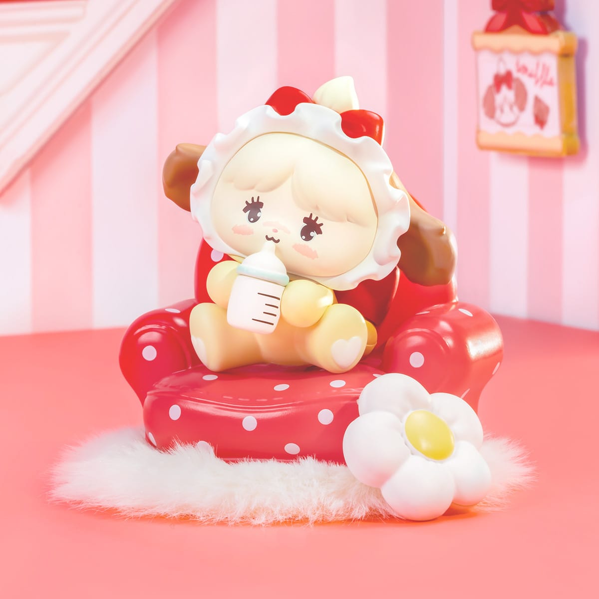 A figure of a cute anthropomorphic dog wearing a bonnet and holding a bottle of milk. It is wearing aright red bow and sitting on a red chair.