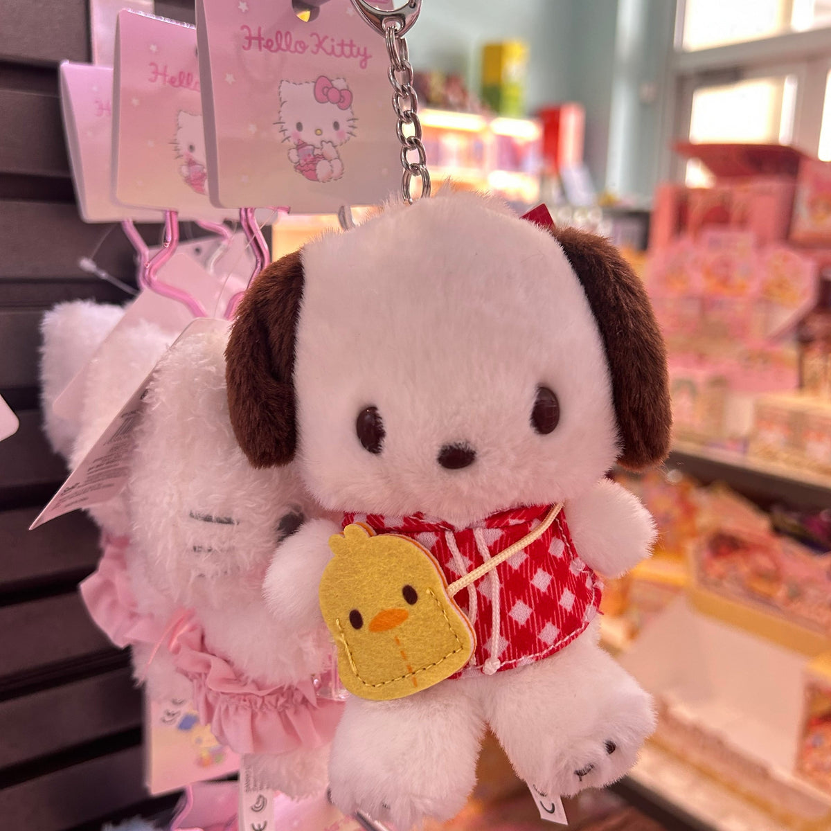 A Pochacco plush key chain. He is wearing a red sweater, and is holding a baby chick.