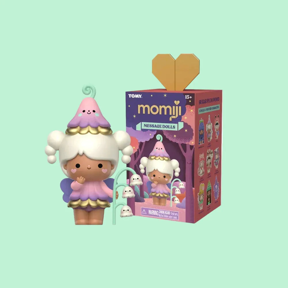 A cute figure of a girl dressed as a flower stood beside a blind box of other cute figures in forest themed outfits.