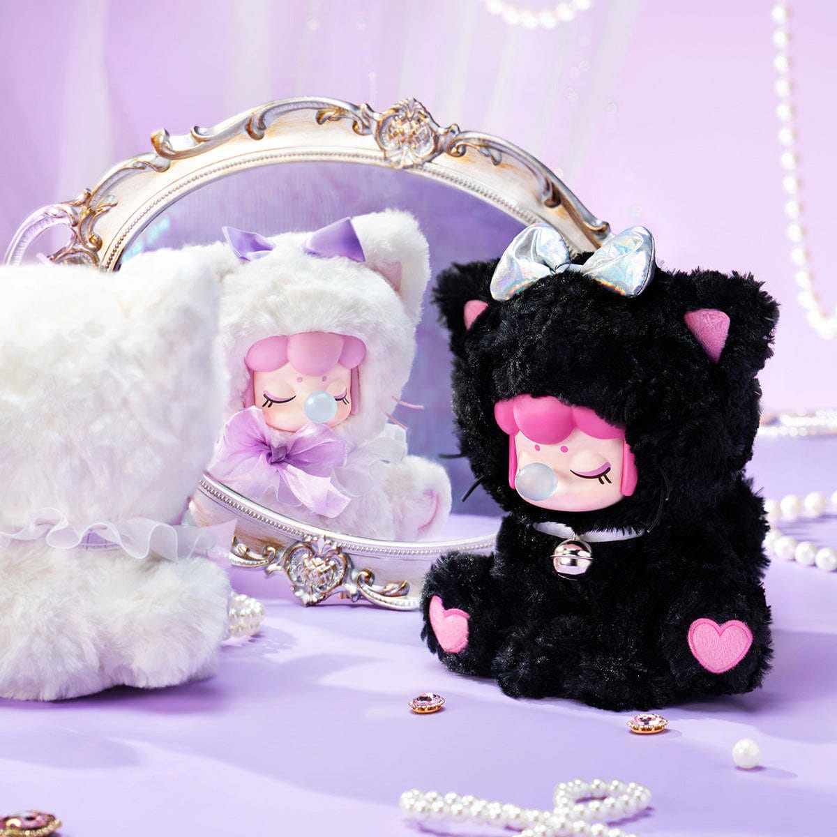 A figure of a little girl wearing a black fluffy cat onesie. She is blowing a bubble and sitting next to another figure wearing a white cat onesie.
