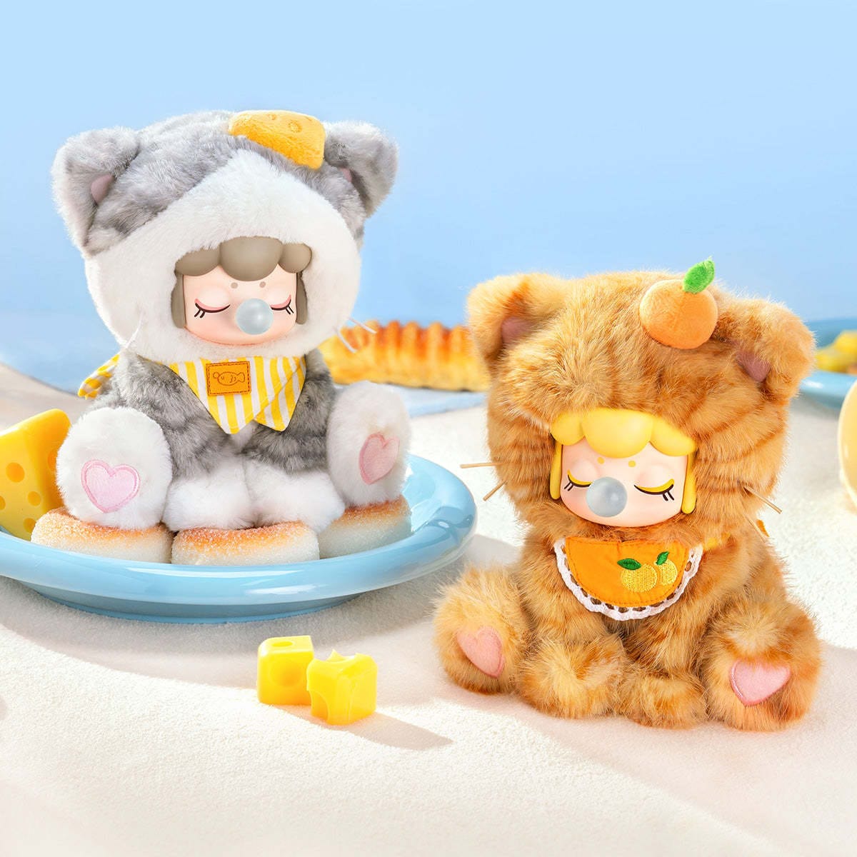 Two figures of little girls in fluffy cat onesies. One cat onesie is orange while the other is gray.