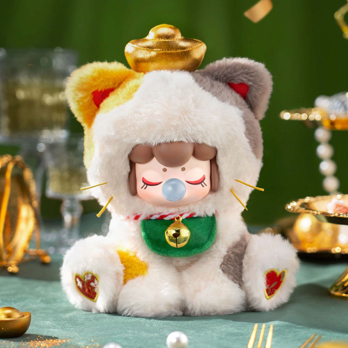 A figure of a little girl in a calico cat onesie. She is blowing a bubble and wearing a little bell.