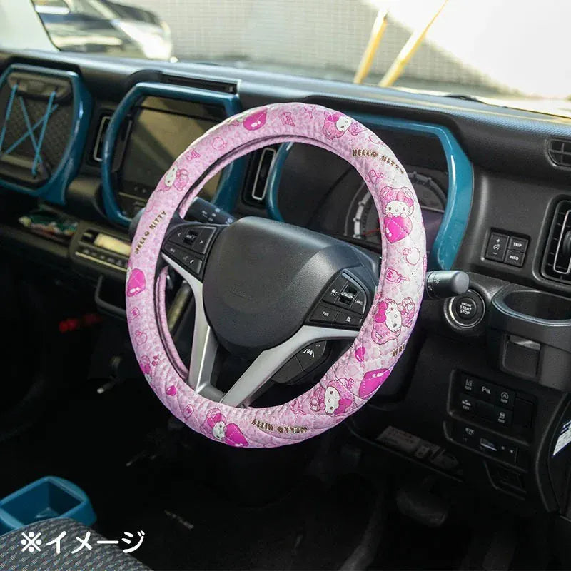 A steering wheel with a pink cover on it. The cover has various illustrations of Hello Kitty on it.