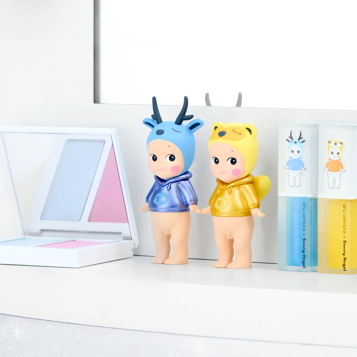 On a vanity stand two sonny angels, one blue deer and the yellow tanuki.