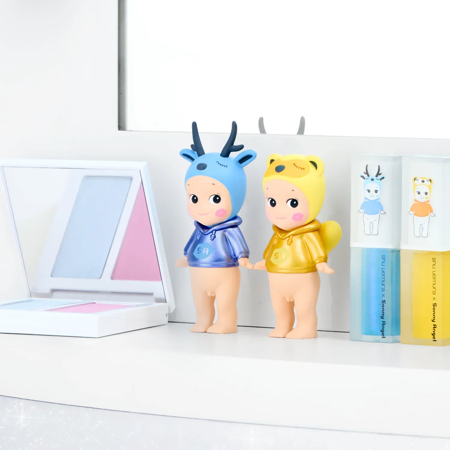 On a vanity stand two sonny angels, one blue deer and the yellow tanuki.