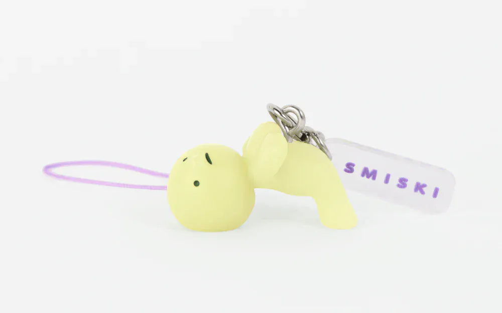 A keychain of a simple cartoon man leaning over backwards to balance on his feat and oversized head. There is an attached tag which says Smiski in purple text.